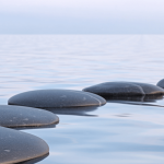 a row of flat black rocks on a peaceful body of water for post called 9 easy self-care tips to reduce stress