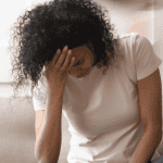 stressed woman sitting on couch with head bent over in her hand.