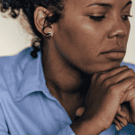 Middle aged woman thinking with hands crossed under chin and tension in face for post called 7 self-care tips to stop negative thoughts and anxiety.