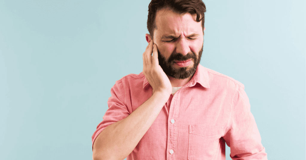 man in pink shirt holding ear