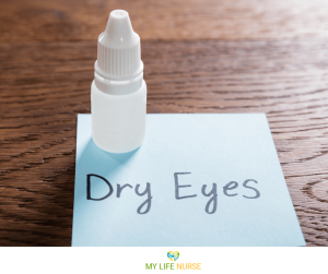 blue sticky note on wooden table with 'dry eyes' written on it, with an eye drop bottle nearby.